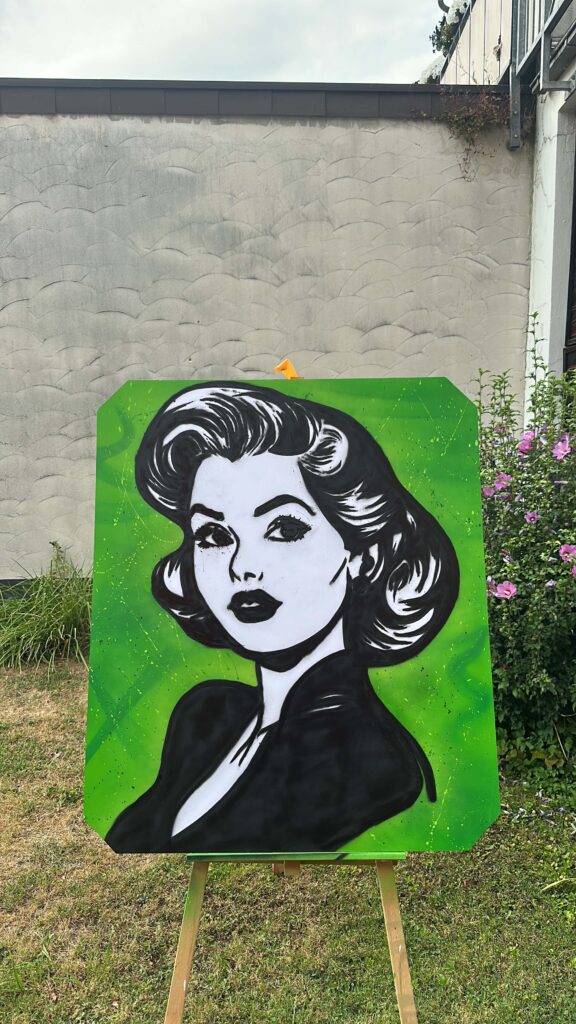 Graffiti-Kunst von Graugegner: schwarz-weißes Frauenporträt mit gewelltem Haar vor grünem Hintergrund auf einer Staffelei.