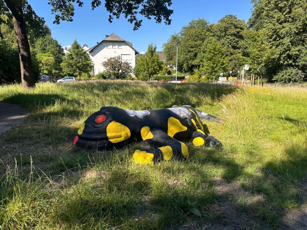 Objektgestaltung von Graugegner: große schwarze Salamanderfigur mit gelben Flecken und roten Augen auf einer Wiese.